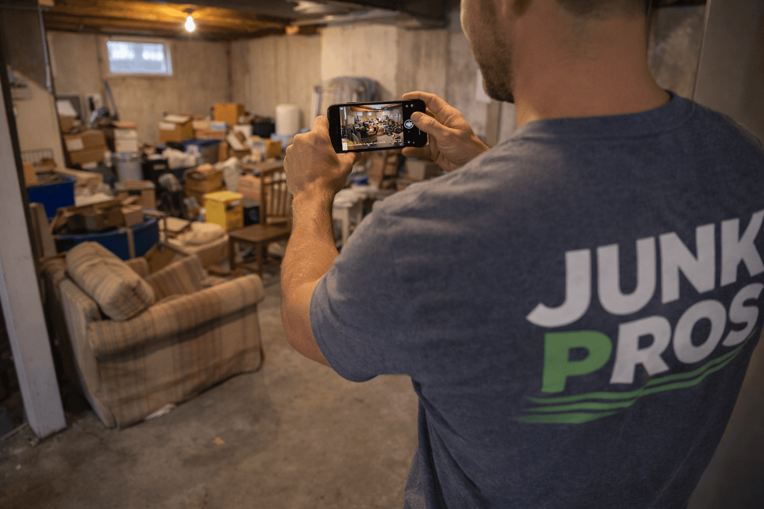 Junk hauler taking a before photo of a cluttered basement with his smartphone